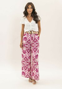 Chemisier blanc avec des manches courtes volantes, associé à un pantalon large rose et blanc à motifs floraux et poches.