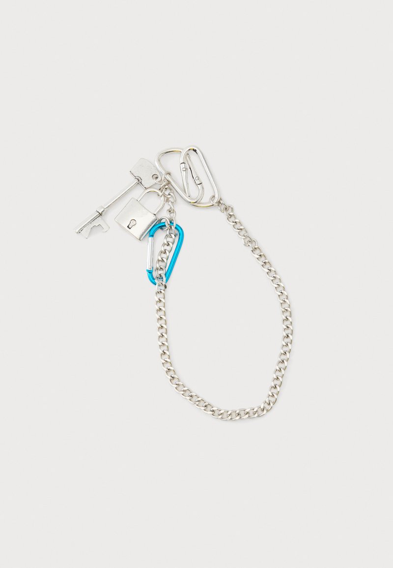Chaîne en argent avec breloques clés et cadenas en argent, attachée à des mousquetons argentés et bleus sur un fond blanc uni.