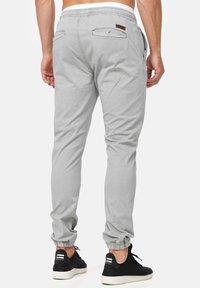 Pantalones de chándal grises con cintura elástica, piernas ajustadas y dos bolsillos traseros. Combinados con zapatillas deportivas negras con suelas blancas.