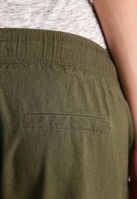 Olive green pants with a soft texture, featuring an elastic waistband and a single back pocket with straight stitching detail.