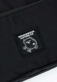 Musta kangas, jossa on ommeltu läppä, jossa on outo pörröinen hahmo ja valkoiset tekstit "Nordicbuddies Clothing Co.".