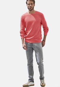 Koralfarbenes Strickpullover mit langen Ärmeln, kombiniert mit hellgrauen Jeans und zweifarbigen Sneakers mit weißen und braunen Akzenten.