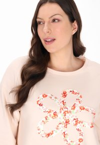 Hanorac roz cu un design floral supradimensionat în nuanțe de portocaliu și alb, cu o textură moale și o gatură lata.