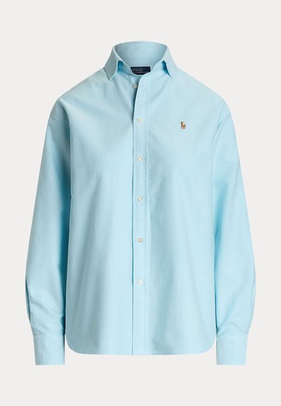 Šviesiai mėlyna marškinė su klasikine apykakle, ilgomis rankovėmis ir baltomis mygtukais. Yra mažas siuvinėtas logotipas ant kairiojo krūtinės.