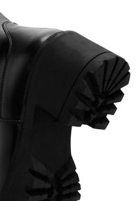 Czarne skórzane botki za kostkę z grubą gumową podeszwą, charakteryzującą się wyraźnym wzorem bieżnika dla lepszej przyczepności i wsparcia, podkreślającymi trwałość i przyczepność.