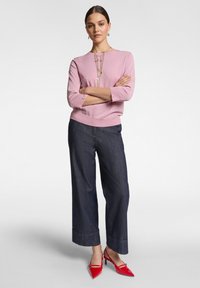 Maglione lavorato a maglia di un rosa chiaro con maniche a tre quarti, abbinato a pantaloni cropped a gamba larga in denim scuro e décolleté rossi a punta.