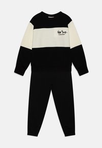Completo di felpa e pantaloni in blocco di colore nero e crema. La felpa presenta un collo rotondo e un logo, abbinata a pantaloni neri a gamba affusolata con polsini elasticizzati. Composizione in miscela di cotone.