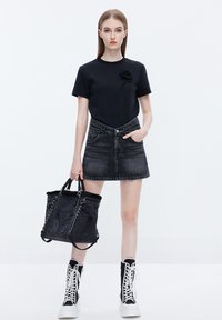 Camisa negra de manga corta con un detalle de flor, falda de mezclilla negra, bolso tote negro con ribete de piel de pelo y zapatillas altas en blanco y negro.