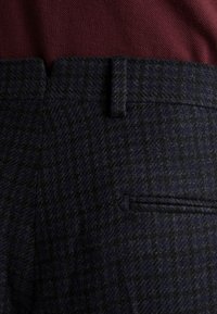 Ciemnoniebieskie spodnie wykonane z teksturowanej tkaniny w wzór w pieszą kratę, z paskami oraz boczną kieszenią o eleganckim designie.