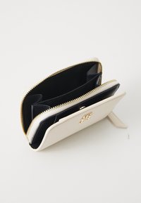 Portefeuille en cuir blanc avec fermeture éclair en or et logo. Dispose d'un intérieur marine avec plusieurs emplacements pour cartes et un compartiment spacieux.