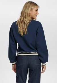 Felpa blu navy con vestibilità comoda, polsini e banda in vita a coste, con strisce crema e nere. Realizzata in un tessuto morbido con una texture liscia.