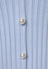 Hellblaues geripptes Strickkleidungsstück mit zwei auffälligen Perlenknöpfen in der Mitte. Der Stoff hat eine weiche Textur und vertikale Streifen.