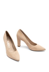 Pompe beige in suede con tacco alto, con punta affusolata e tacco a blocco di altezza media. Tessuto liscio con un dettaglio cucito lungo l'apertura.