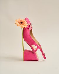 Chaussure compensée en daim rose avec un design découpé, sangle de cheville réglable et boucle décorative, positionnée avec une fleur.