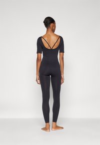 Crni bodysuit s rukavima srednje dužine, otvorenim leđima s ukrštenim trakama, dizajn koji prianja uz tijelo, glatka tekstura, uparen s odgovarajućim tajicama.