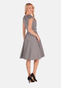 Schwarz-weiß kariertes Kleid mit kurzen Ärmeln, tailliertem Oberteil und A-Linie-Rock. Mit einem taillierten Gürtel und seitlichen Taschen. Getragen mit schwarzen Absätzen.