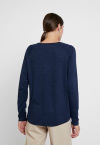 Maglione a maniche lunghe blu navy realizzato in tessuto morbido; presenta un collo a girocollo e maniche raglan, con un orlo leggermente curvo.