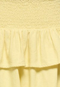 Tissu jaune avec des fronces smockées en haut et un détail de volants froncés en dessous, créant texture et volume.