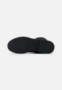 Suela de zapato negra con un patrón de agarre texturizado, tamaño 39, fotografiada desde abajo sobre un fondo blanco.