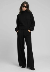 Pull à col roulé en tricot noir associé à un pantalon noir à jambes larges. Les deux vêtements présentent une coupe décontractée et le pull est doté de poches à main.