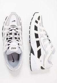 Nike tenisky se síťovaným a syntetickým svrškem v bílé a šedé barvě, s černými akcenty, zaoblenou špičkou a kontrastní gumovou podrážkou s trakčním vzorem.