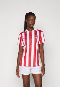 Crveno-bijela prugasta nogometna majica kratkih rukava s ovratnikom i logom Atletica Madrida. U paru s bijelim kratkim hlačama s Nike logom.
