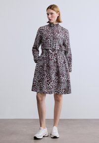 Φόρεμα με λεοπάρ μοτίβο, ψηλό γιακά, κλείσιμο με φερμουάρ, ζώνη στη μέση και τσέπες. Κατασκευασμένο από υλικό με υφή, με φούστα μήκους μέχρι το γόνατο.