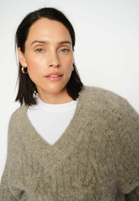 V-kaelusega, lahtise lõikega kampsun pehmest, soojast hallist materjalist, millel on kollased täpid. Kantakse valge T-särgi peal, millel on soonilised detailid.