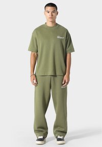 Oliivinvihreä yhtenäinen asu, joka on valmistettu pehmeästä kankaasta, sisältää rento t-paita lyhyillä hihoilla ja löysät housut.