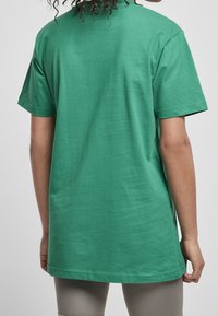 Camiseta de algodón verde con mangas cortas, cuello redondo y corte holgado, con una textura suave y un diseño liso sin adornos.
