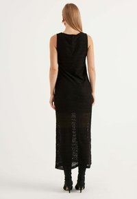 Abito maxi nero senza maniche realizzato in tessuto testurizzato con motivo a zigzag; presenta una silhouette lunga e aderente e una leggera trasparenza all'orlo.