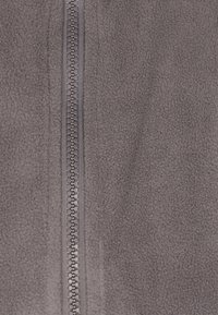 Tessuto in pile grigio con una texture liscia, dotato di una cerniera centrale con denti interbloccati. Design minimalista senza motivi o dettagli.