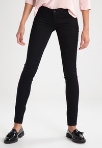 Vaqueros skinny negros hechos de una tela elástica, con un diseño clásico de cinco bolsillos y costuras sutiles. Combinados con mocasines negros.