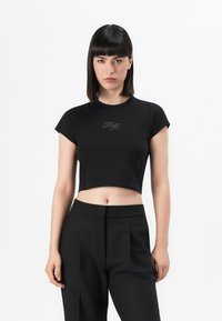 Melnā īsā t-kreklā ar īsām piedurknēm, kas rotāta ar mirdzošu "Fizzy" tekstu dizainā no rhinestones, centrēta uz krūšu daļas.