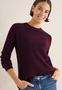 Bordeaux gebreide trui met een geribde textuur en ronde halslijn, gecombineerd met blauwe jeans. Beschikt over lange mouwen en een relaxte pasvorm.