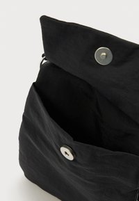 Μαύρη υφασμάτινη τσάντα με υφή στην επιφάνεια, διαθέτει κλείσιμο με μαγνητικό κουμπί και ευρύ άνοιγμα που αποκαλύπτει ευρύχωρο εσωτερικό.