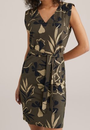 Robe sans manches vert olive avec imprimé floral et feuillage beige et noir, col en V, et ceinture assortie en tissu nouée à la taille.