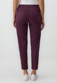 Pantalons bordeaux ajustés avec poches latérales, une texture lisse et une taille mi-haute, associés à des baskets blanches.
