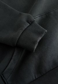 Tamsiai pilkas džemperio audinys su gipiūro rankovėmis. Tekstūra yra minkšta ir lygi, su sustiprintais siūlais palei siūles.