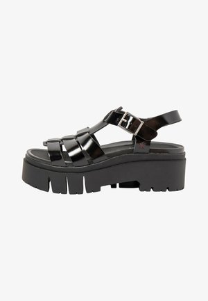 Black patent leather platform sandal with chunky lug sole, multiple straps, and adjustable silver buckle on ankle strap.
