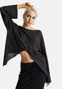 Czarna, lekka bluzka z długim rękawem w stylu odkrytych ramion, z teksturowanym wzorem i zaokrąglonym dołem. Połączona z ciemną spódnicą.
