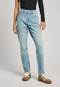Lichtblauwe hoge taille spijkerbroek met een relaxed fit, met vijf zakken en een ritssluiting. Gecombineerd met gestreepte bruin en witte sneakers.
