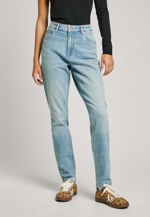 Jeans de mezclilla de tiro alto en azul claro con un corte relajado, que cuentan con cinco bolsillos y un cierre de cremallera. Combinados con zapatillas de deporte de rayas marrones y blancas.