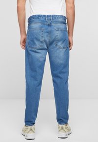 Vaqueros de denim azul con un corte relajado, diseño de cinco bolsillos y un acabado ligeramente desgastado. Presenta una cinturilla y puños elásticos en los tobillos.
