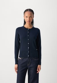 Marineblauwe cardigan van zachte gebreide stof, met een ronde halslijn, knoopsluiting en lange mouwen. Gecombineerd met donkere denim broek.