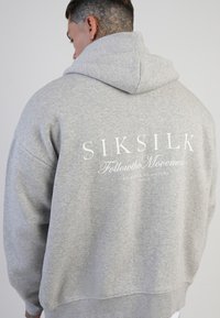 Szara bluza z kapturem o luźnym kroju. Tekst na plecach zawiera "SIKSILK" i "Follow the Movement" na białym tle. Materiał z mieszanki bawełny.