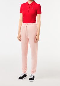 Camisa polo de rayas rojas con cuello y tres botones, combinada con pantalones jogger rosa suave con cinturilla elástica y bolsillos laterales. Zapatillas de deporte negras.