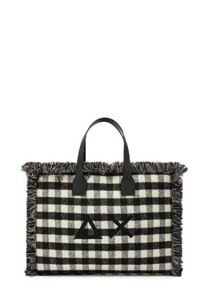 Borsa tote a scacchi bianco e nero con bordi sfilacciati, dotata di manici in pelle nera e un logo al centro. Texture e design distintivi.