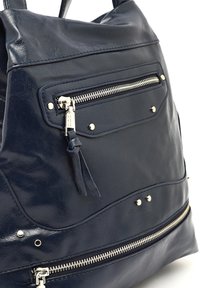 Mornarsko modra torba iz sintetičnega usnja z več žepi na zadrgo, srebrnimi dodatki in teksturirano površino. Vključuje dekorativne kovinske stožce.