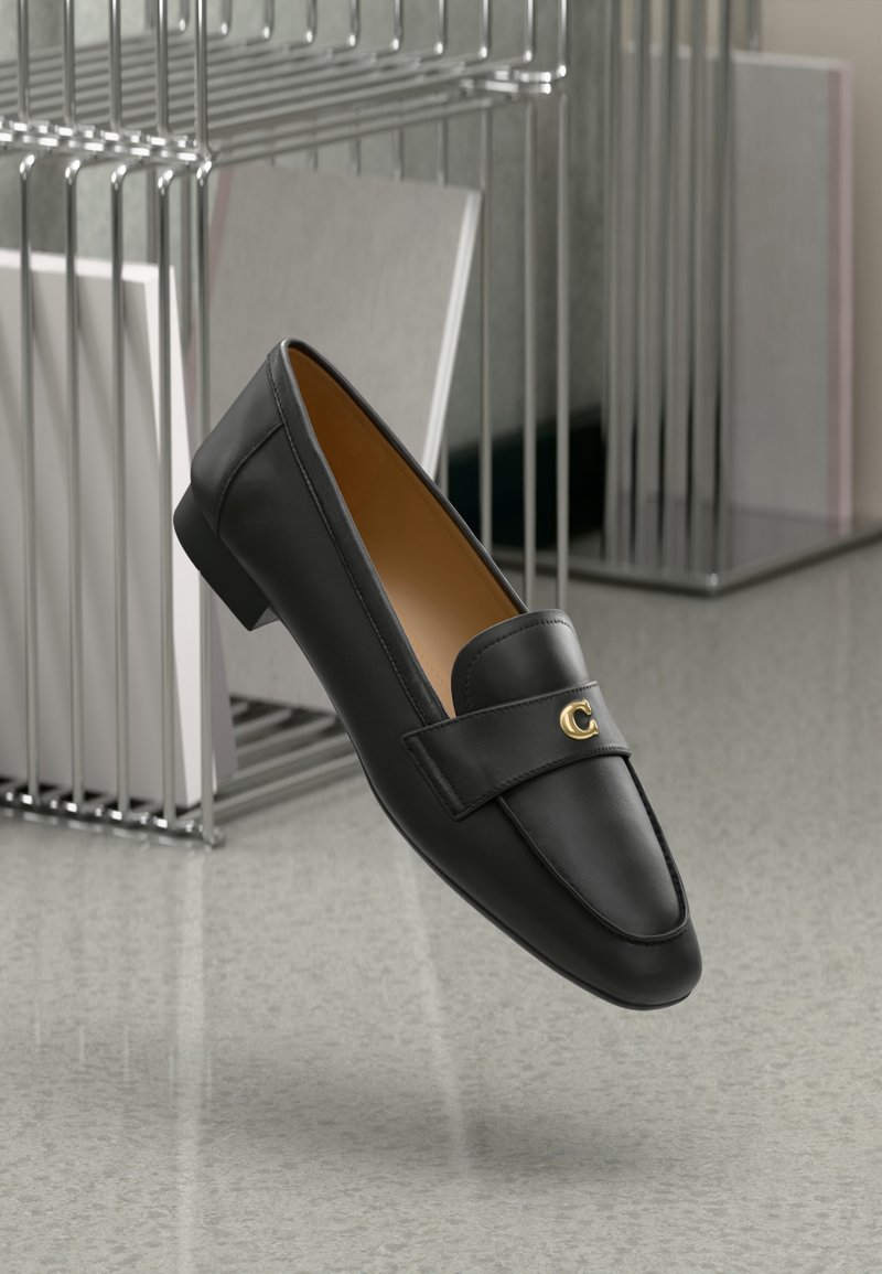 Black leather loafers featuring a gold accent, a rounded toe, and a smooth texture, suspended above a reflective surface with metallic shelving.